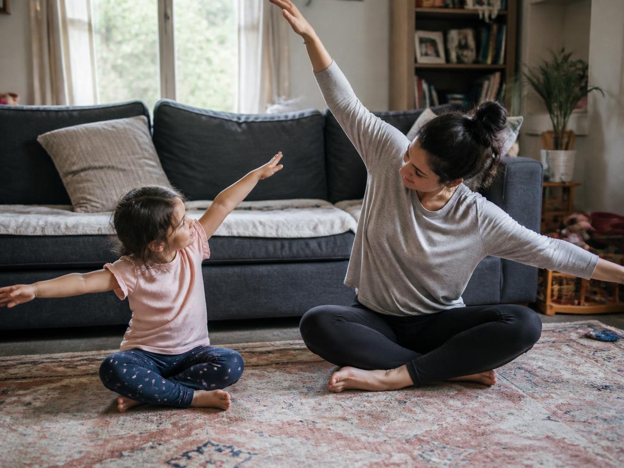 A parent and young child stretching and copying each other's arm movements on a living-room floor